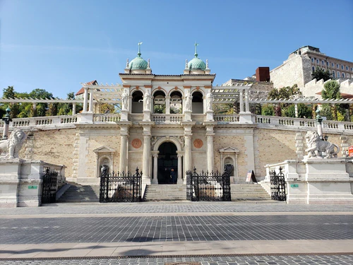Kastelya Bahçesi Pazarı veya Várkert Bazár, Budapeşte Kalesi’nin ayaklarında, Buda Kalesi’nin uçurumunda zarif Miklós Ybl dokunuşuyla master bir 19. yüzyıl kıyı kompleksidir. Tarihi bir canlandırma hazinesi olan bu alan, zarif pavyonlar, basamaklar ve terasları lüks bahçelerle birleştirir; bugün sergiler, konserler, kafeler ve kültürel etkinlikler için ev sahipliği yapar. Mimari ihtişamı, panoramik Tuna ve Buda tarafı manzaraları için ziyaret edilmeye değer; kaleye kolay erişim sağlar, nehir kenarında zarif bir yürüyüş, fotoğraflık cepheler ve Budapeşte’nin tarih ile çağdaş kültürü bir araya gelen kentsel yenilenmesini keşfetme deneyimi sunar. — Tarihî site, rated 4.6/5