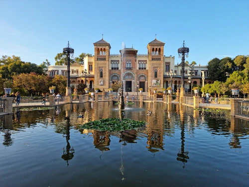 Naast Sevilla’s Guadalquivir toren de Torre del Oro, een 13e-eeuwse maritieme wachttoren die ooit de rivierentree van de stad bewaakte en de goudtransporten uit de Amerikas bewaakte. Haar honingkleurige bakstenen cilinder, bekroond met een octagonale lamp, blijft een van Sevilla’s meest herkenbare bezienswaardigheden. Vandaag herbergt het het Natuur- en Zeemuseum, waarin Sevilla’s zeevaartgeschiedenis van oude handelsroutes tot moderne verkenning wordt belicht. Bezoekers kunnen de exposities verkennen, de gouden vergulde kompas bewonderen die de toren zijn naam gaf, en genieten van uitzicht over de rivier en het maritieme erfgoed van de stad. in Seville — Park